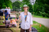 Photo of Brennan standing in front of group of students working in archaeological trenches.