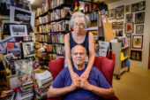 Photo of Gerald McWorter seated in his home library with his wife, Kate Williams, standing behind him with her arms around his neck.