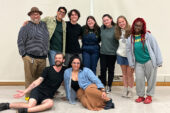 Photo of a group of people standing together, with two people seated in front.