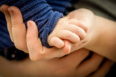 Adult's hand cradling a toddler's hand