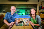 The researchers in a laboratory. Between them is a fish tank with an octopus inside that has been placed in the temporary tank for the photograph.