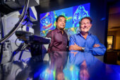 Two men in front of projected microscope images.