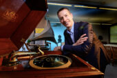 Photo of John Paul Meyers dressed in a suit and leaning toward a Victrola record player.