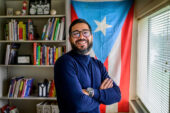 Photo of Omar Pérez Figueroa in his office with a Puerto Rican flag hanging in the background.