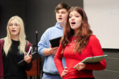 Photo of three students singing, all of them holding tablet computers.