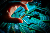 A researcher is holding a vial of gold that has been extracted from disgarded electronics in the background