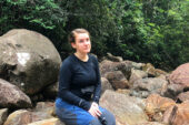 Graduate student Emma Lundin sitting on a boulder with the forest behind her