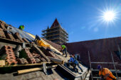 Photo of workers on the slop of Altgeld Hall's roof with the bell tower in the background and tiles piled on wooden planks on the roof.