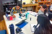 Three engineering students seated around a table work on a team project in the classroom.