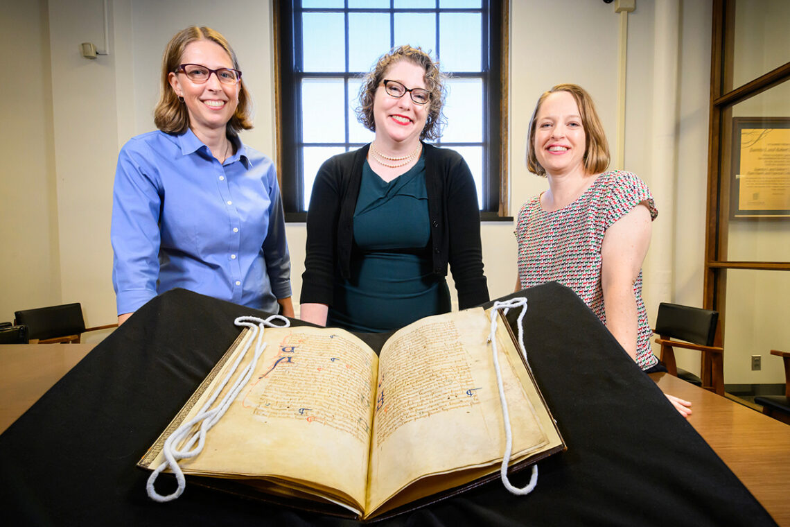 Photo of Sarah C. Williams, Lynne M. Thomas and Erin E. Kerby surrounding a medieval manuscript copy of Walter of Henley's "Hosbondrye."