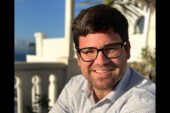 Headshot of Eric Calderwood with a white railing and building and a palm tree in the background.