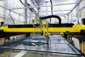 Image shows a large industral 3D printer depositing ink composite on to a surface