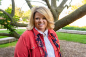 Nancy Latham standing outdoors in front of a small tree wearing a jacket and scarf