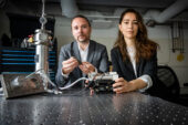 Researchers seated at table with instrument used to perform their new metal fatigue testing methodoloy