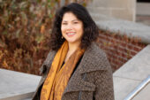 Photo of social work professor Lili Windsor standing in front of a campus building wearing a winter coat and long scarf