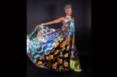 Full-length image of Cynthia Oliver in a long, colorful dress, holding out one side of her skirt.