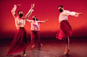 Image of three dancers on stage in white tops and flowing red skirts.