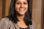 Mina Raj smiles at the camera, wearing a tan blazer over a blue top.