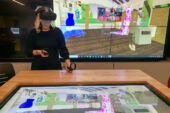 Art professor Chiara Vincenzi wearing virtual reality goggles and standing in front of a screen displaying dresses in a virtual world.