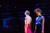 Image of two dancers standing at the right of a stage.