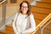 Photo of U. of I. professor Karen Kramer standing at the bottom of a stairway and leaning on one elbow on the railing
