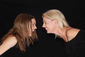 Photo of mother and daughter bending toward each other and smiling widely