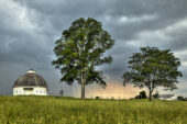 Storm clouds behind a round barn and tree