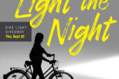 Silhouette of a person standing with a bike with a light shining from the headlight