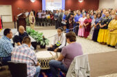 Men playing a drum in the foreground, with dignitaries and speakers standing to honor their performance
