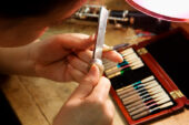 Oboe major Amelia Lee uses a knife to refine an oboe reed. On the table, her reed case is filled with reeds in various stages of completion.