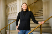 Christina Kamis standing on a staircase in a campus building holding onto the handrail.
