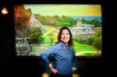 Photo of researcher standing in front of a photo of the remains of an ancient Maya city.