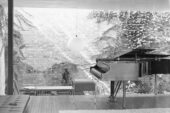 Black and white photo of a grand piano sitting in a room with a brick wall lit by the sun in the background.