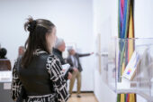 Photo of a woman looking at a textile wall hanging in a gallery.