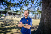 Nick Pitas standing next to a tree in a park with a pavilion in the background.