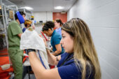 Photo of the author working with a cockatiel that she holds wrapped in a small towel. Other students, instructors are seen working in the background.