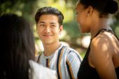 Male and female students talking near the Alma Mater statue on campus.