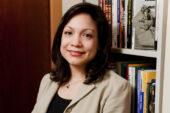 Portrait of Lissette Piedra standing in front of a bookcase wearing a beige jacket and black shirt