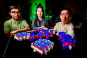 Researchers seated behind a hand scale prototype of their new multilayer material.