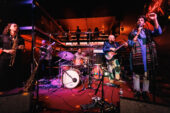 Photo of a band onstage, lit by red light.