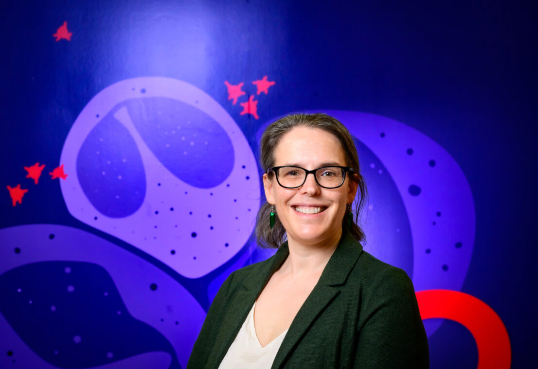 A woman stands in front a mural depicting viruses and cells