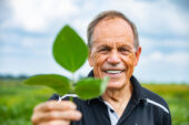Photo of Stephen Long standing in a soybean field and holding a soybean leaf.