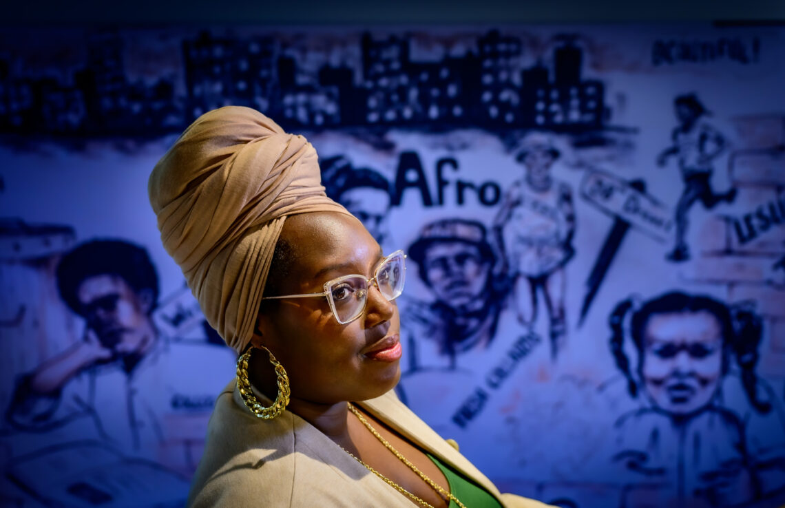 Sociology professor Brittney Miles shown in profile with a Black history mural at the Bruce D. Nesbitt African American Cultural Center on campus.in the background.