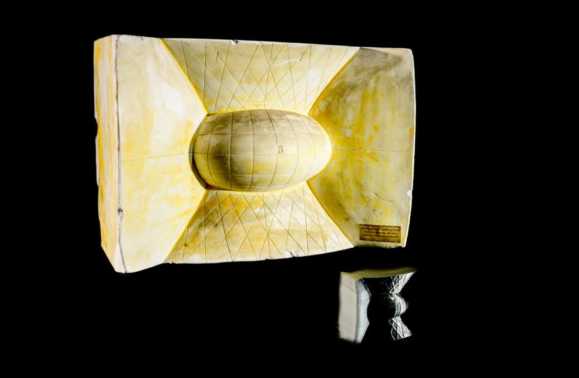 A photo of a plaster model featuring an ellipsoid and two hyperboloids, with a small 3D-printed re-creation of the model.