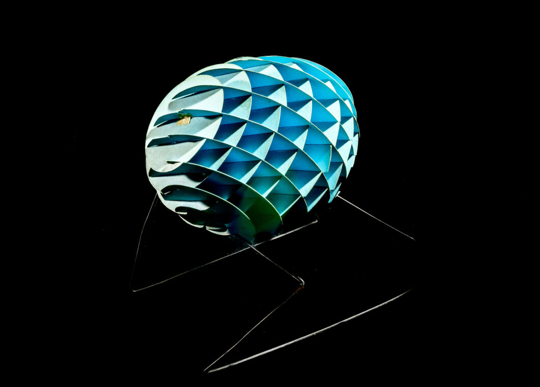 Photo of a blue cardboard ellipsoid made of various circular sections and standing on metal legs.