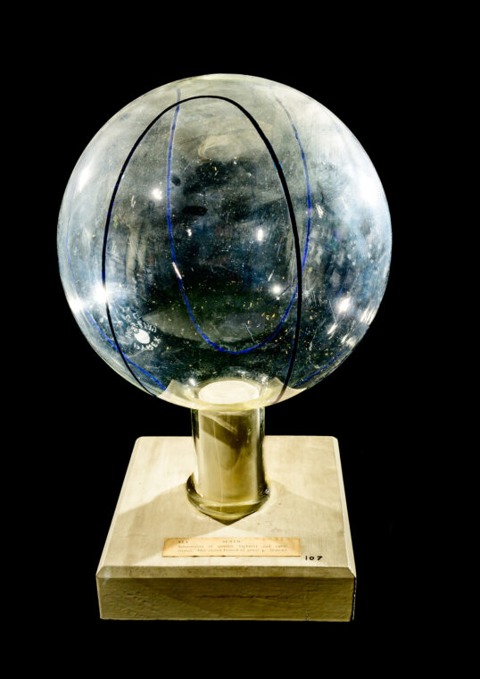 Photo of a clear sphere on a wooden stand with curves marked on the sphere.
