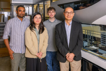 Four people stand in front of a large piece of laboratory equipment
