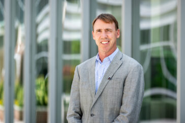 Portrait photo of Paul Hergenrother standing outside a glass-walled building on campus.