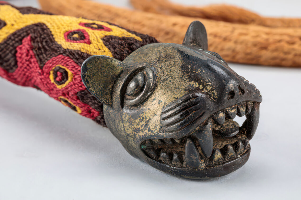 Photo of the end of a colorful braided rope whip from Peru. The end features the head of some type of wild cat.