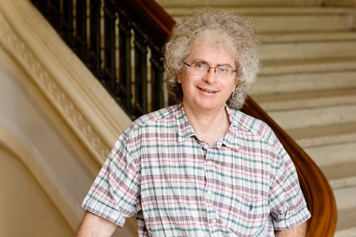 Photo of Richard Tempest standing before a marble staircase with a wooden banister.